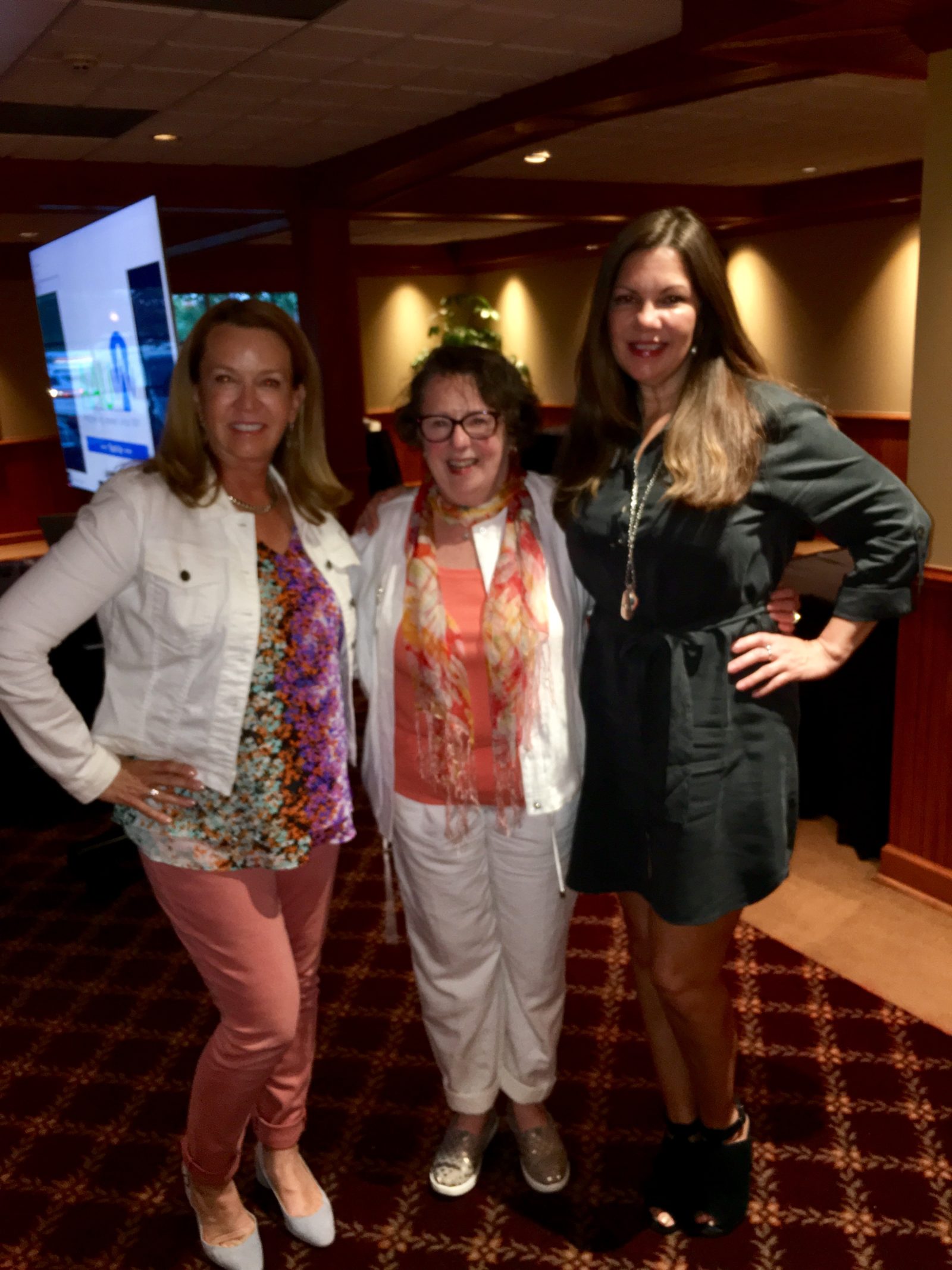 Three smiling women posing in dimly lit lounge