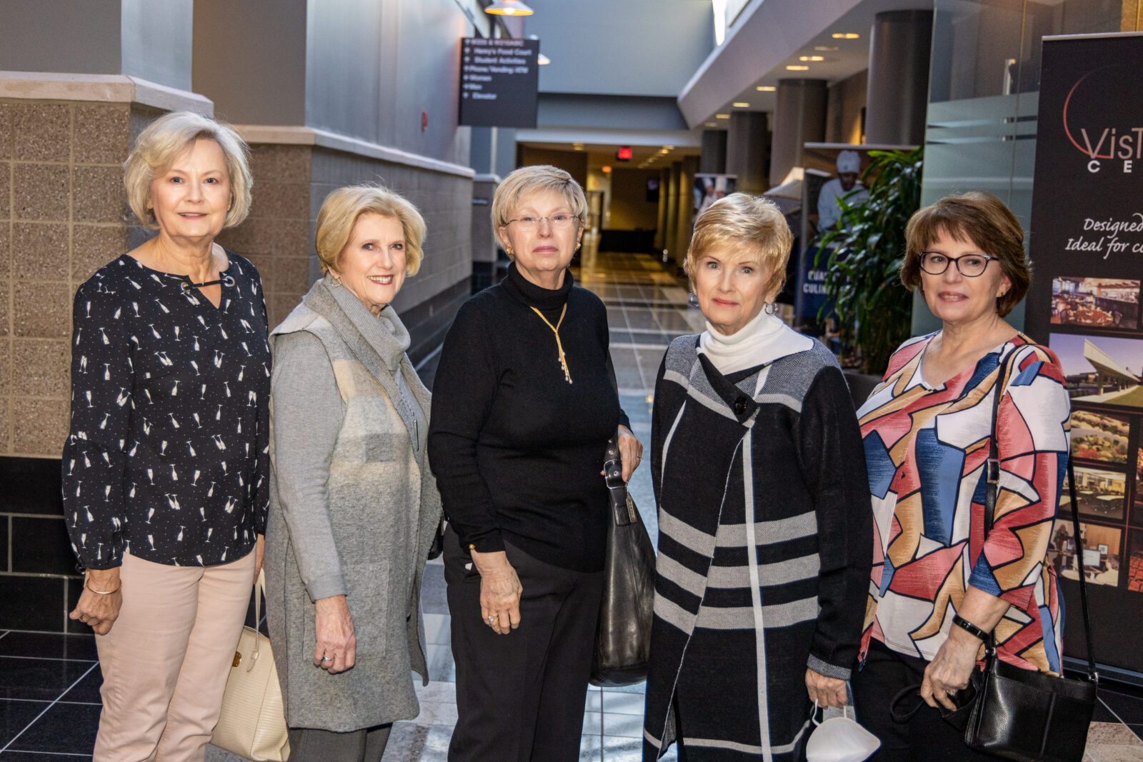 Five women standing in indoor conference hallway